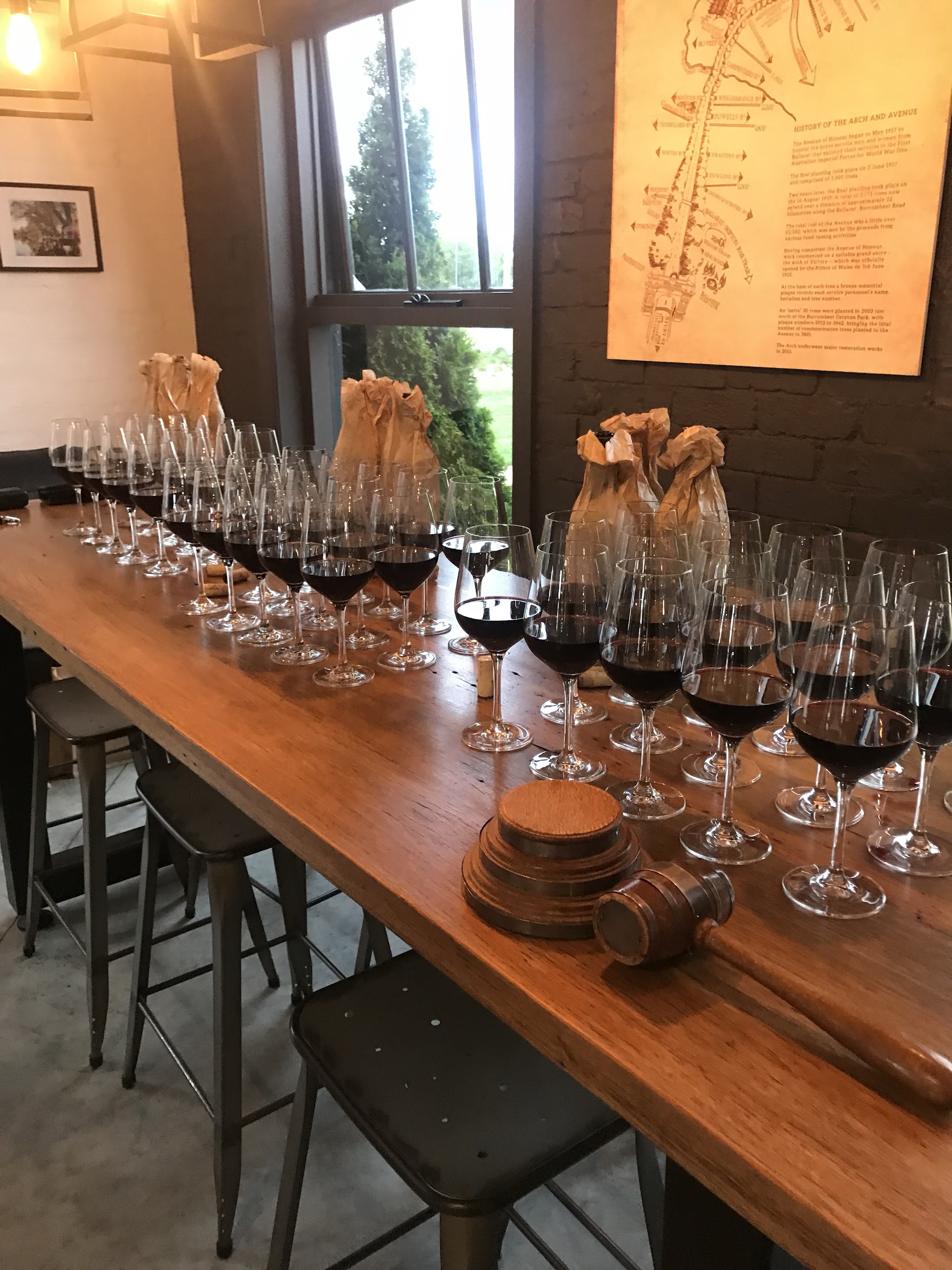 A long timber bar lined with wine glasses beneath a framed history of the Arch and Avenue