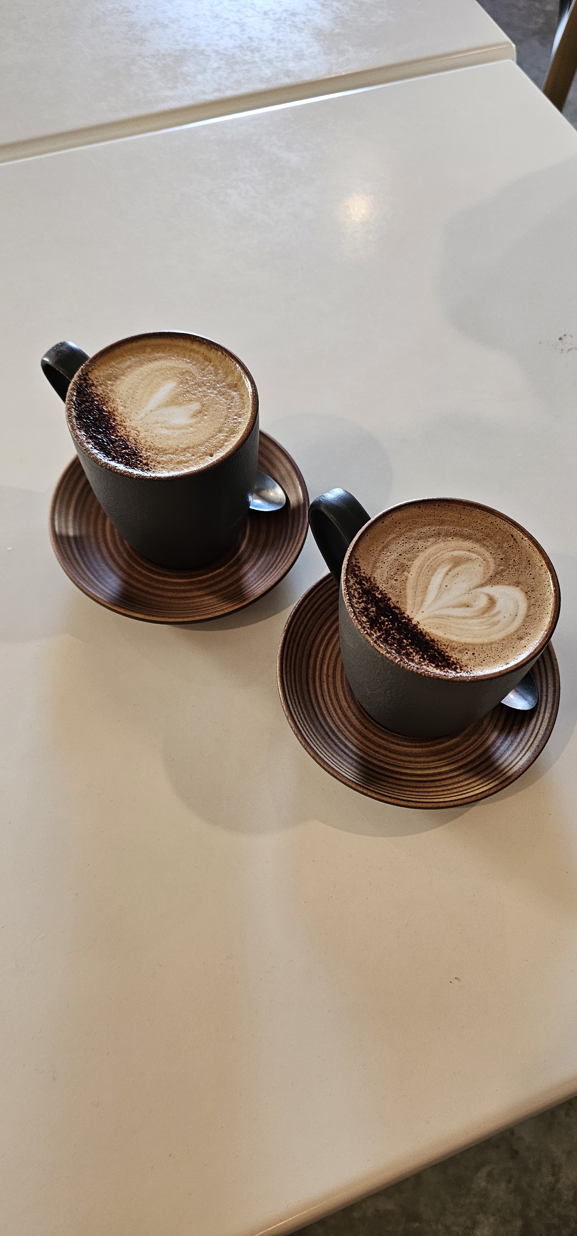 Two flat whites with latte art hearts in dark cups on timber saucers