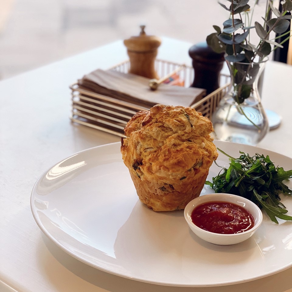 A savoury muffin with relish and rocket on a white plate