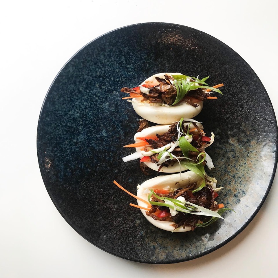 Three bao buns with pulled meat, carrot and spring onion on a dark plate