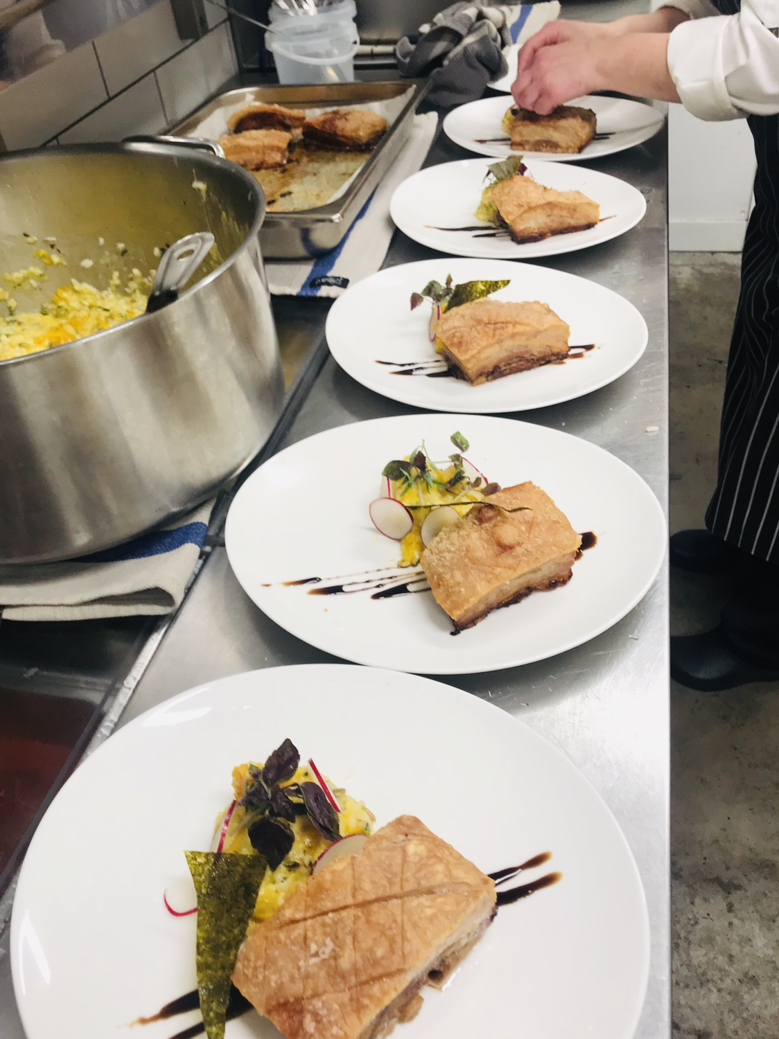 Plates of crackling pork belly being finished in the kitchen