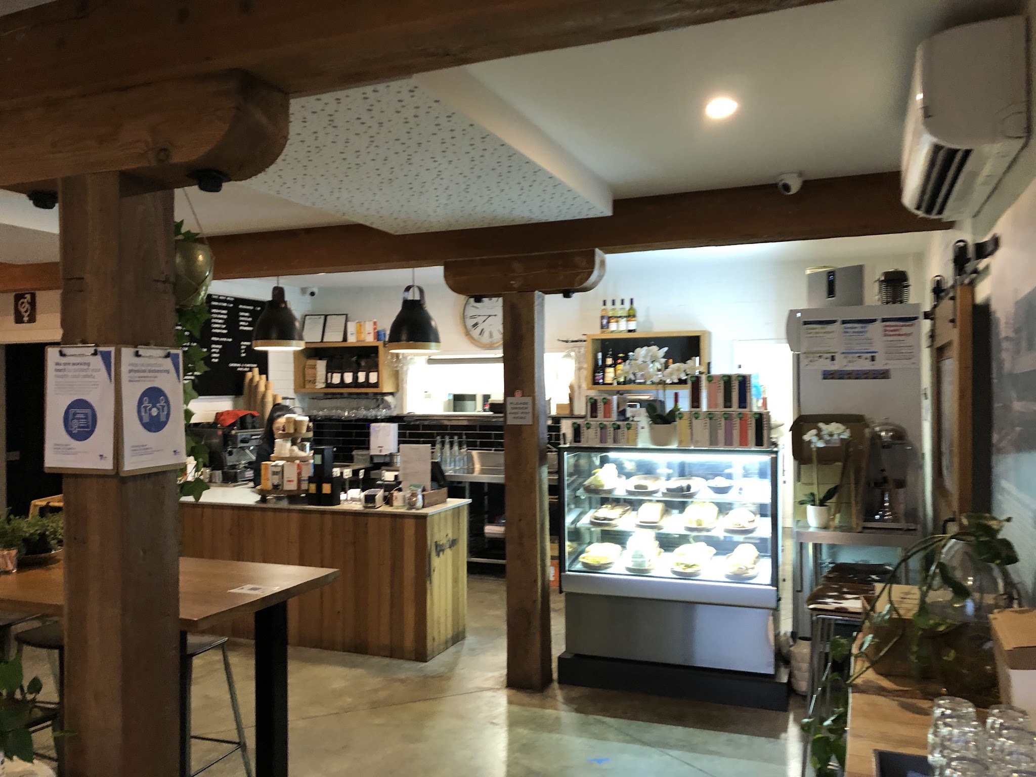 The front counter, espresso machine and lit cake cabinet under timber beams